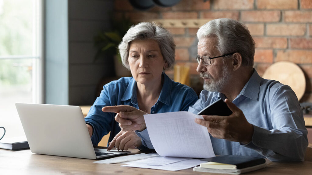 older couple looking at papers and computers with calculator